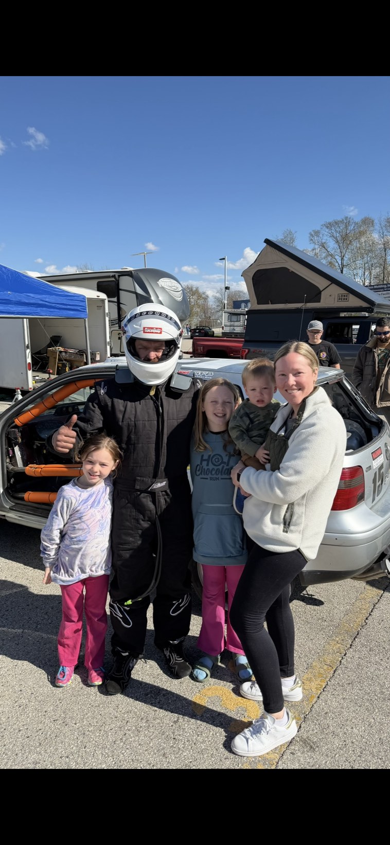 Driver in racing suit with family in pit lane