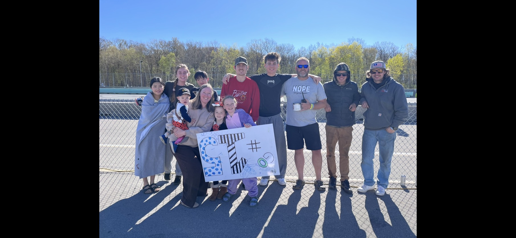 Full team and family group photo with homemade sign at Road America